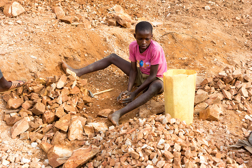 Ugandan boy breaking rocks into small slabs