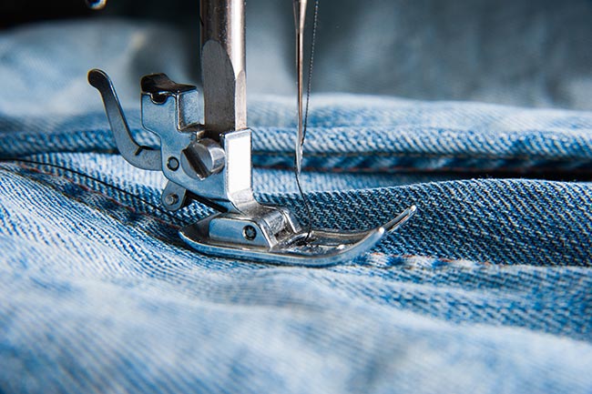 Close-up van een naaimachine naald op jeans. Illustratie bij IMVO Convenant Duurzame Kleding en Textiel.