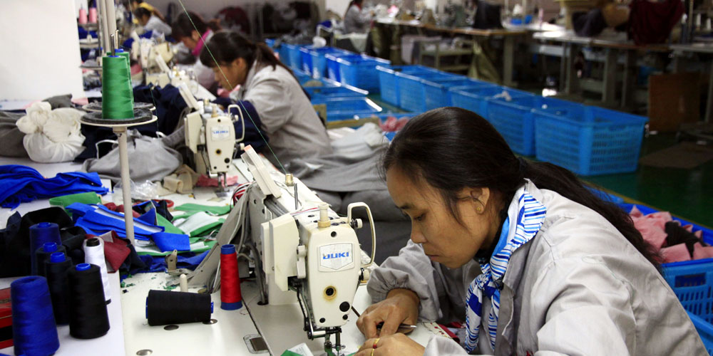 Vrouwen aan het werk achter hun naaimachines in grote fabriek. Illustratie bij IMVO Convenant Duurzame Kleding en Textiel.