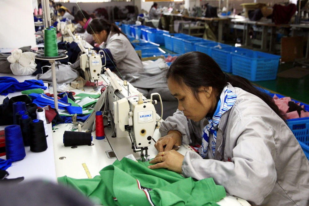 Vrouwen aan het werk achter hun naaimachines in grote fabriek. Illustratie bij IMVO Convenant Duurzame Kleding en Textiel.