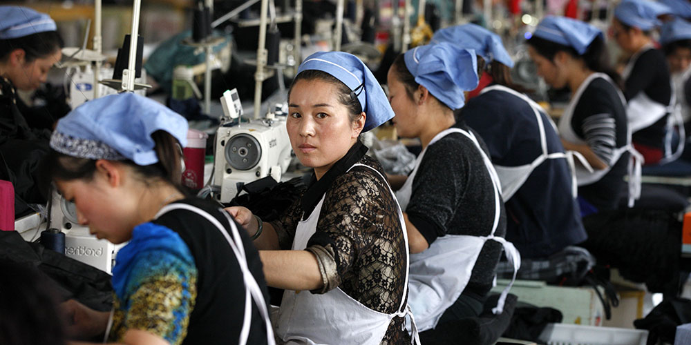 Vrouwen aan het werk achter hun naaimachines in grote fabriek.