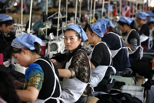 Vrouwen aan het werk achter hun naaimachines in grote fabriek.