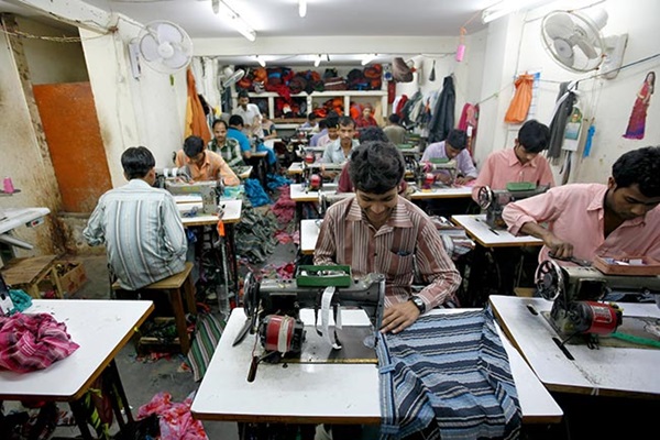 Mannen aan het werk achter hun naaimachines in grote fabriek. Illustratie bij IMVO Convenant Duurzame Kleding en Textiel.